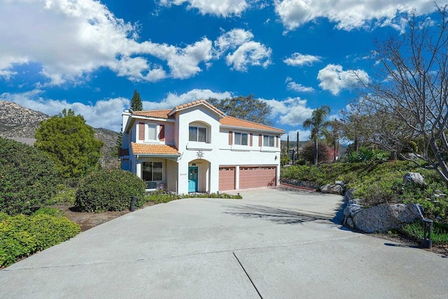 mediterranean / spanish-style house with a garage, stucco siding, concrete driveway, and a tiled roof