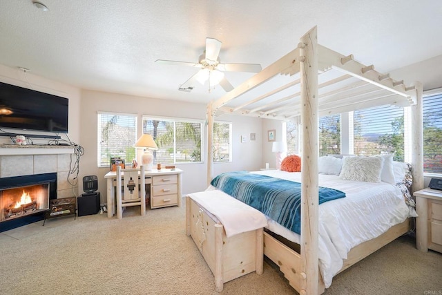 bedroom with ceiling fan, a textured ceiling, a tiled fireplace, and light colored carpet