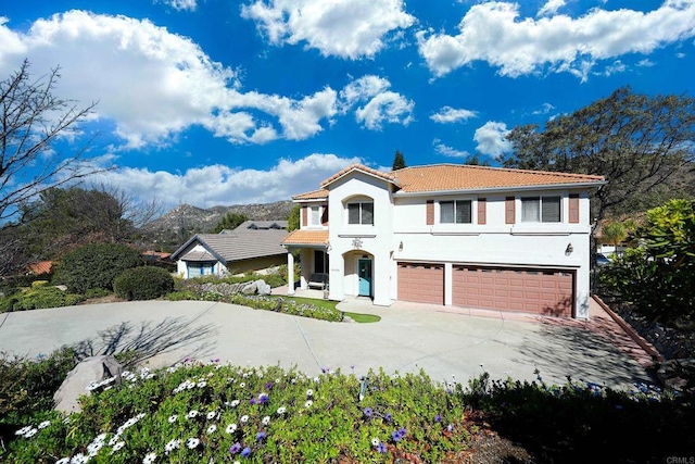 mediterranean / spanish-style home with driveway, an attached garage, a tiled roof, and stucco siding