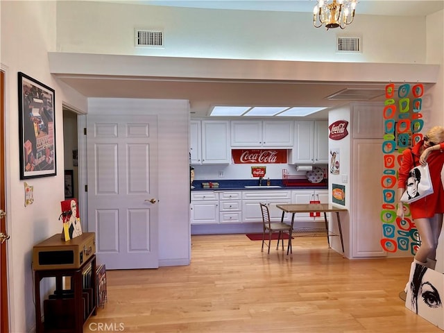 kitchen with light wood-style flooring, visible vents, white cabinets, and a sink