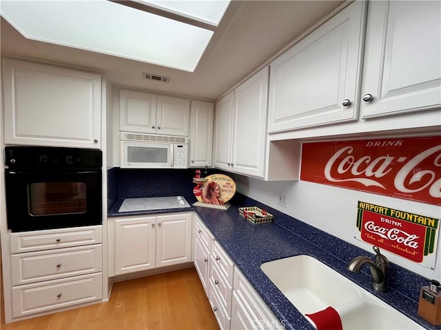 kitchen with visible vents, white appliances, a sink, and white cabinetry