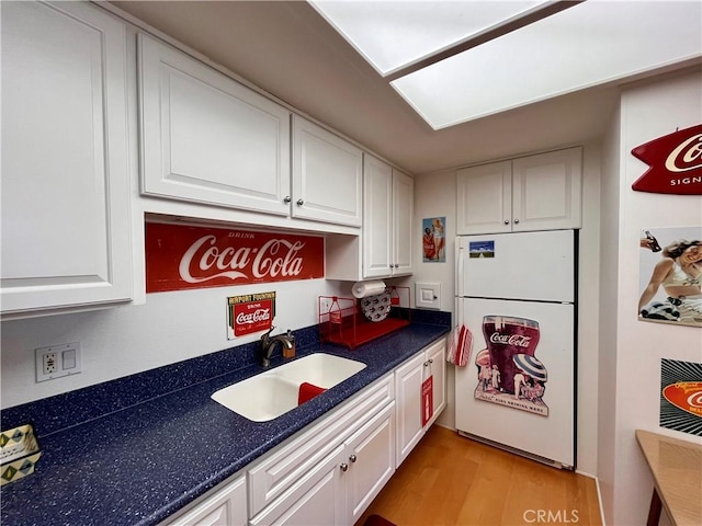 kitchen with white cabinets, dark countertops, light wood-style flooring, freestanding refrigerator, and a sink