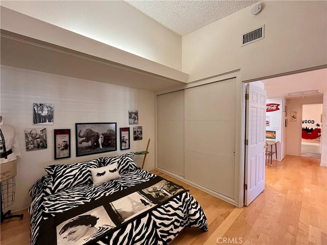 bedroom with light wood-style flooring, a closet, visible vents, and a textured ceiling