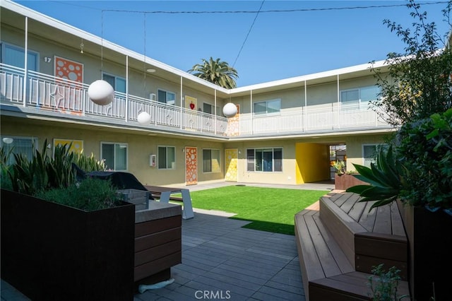 back of house with a lawn, a balcony, and stucco siding