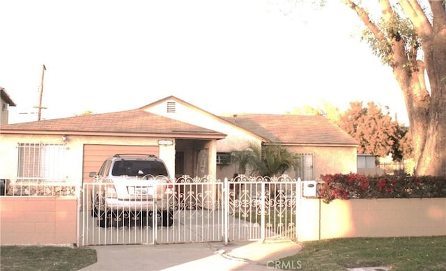 view of front of house featuring stucco siding, a gate, fence, a garage, and driveway