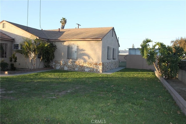 view of side of property featuring a yard, stone siding, fence, and stucco siding