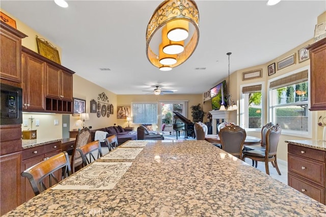 kitchen with ceiling fan, light stone counters, open floor plan, a fireplace, and black microwave