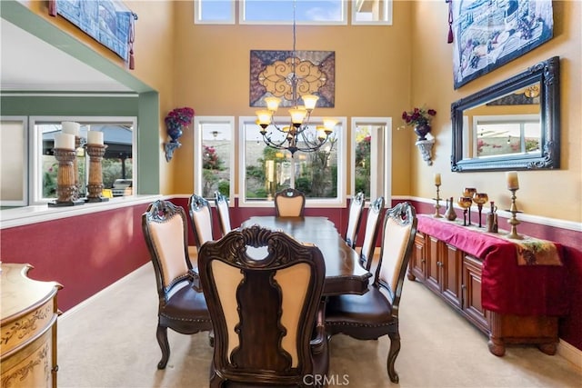 dining area featuring a healthy amount of sunlight, an inviting chandelier, light carpet, and a high ceiling