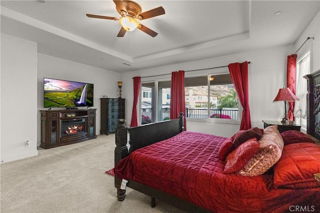 carpeted bedroom with baseboards, a tray ceiling, a ceiling fan, and a glass covered fireplace