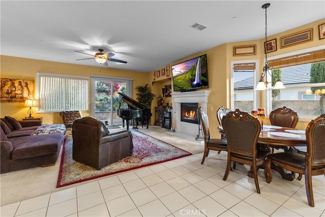 living room featuring a ceiling fan, visible vents, a lit fireplace, and light tile patterned floors