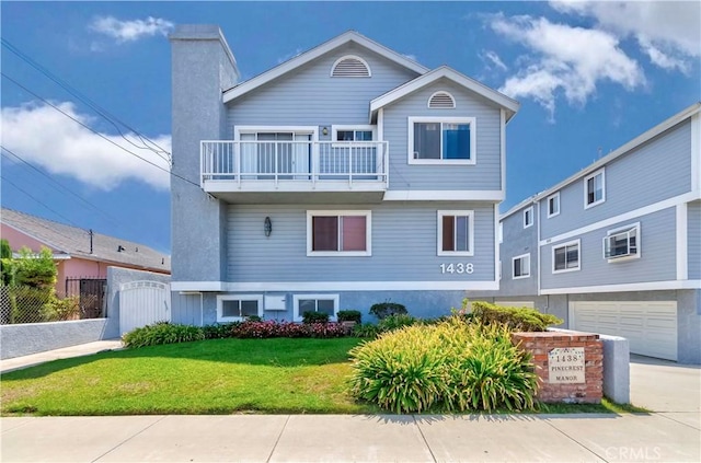 view of front facade featuring driveway, a balcony, fence, a front yard, and stucco siding