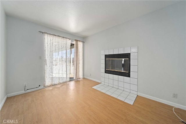 unfurnished living room featuring a textured ceiling, a fireplace, baseboards, and wood finished floors