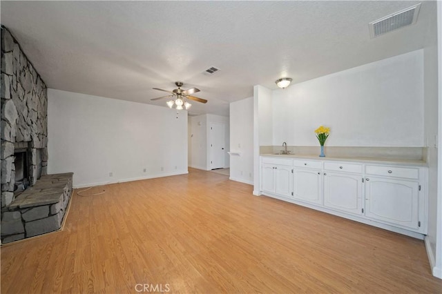 unfurnished living room featuring visible vents, a ceiling fan, light wood-type flooring, a fireplace, and a sink