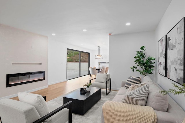 living area featuring light wood-style floors, a glass covered fireplace, baseboards, and recessed lighting