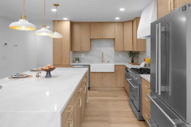 kitchen with high end appliances, wall chimney exhaust hood, light countertops, light wood-type flooring, and a sink