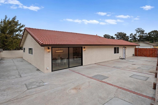 rear view of house with a tile roof, a patio area, fence, and stucco siding