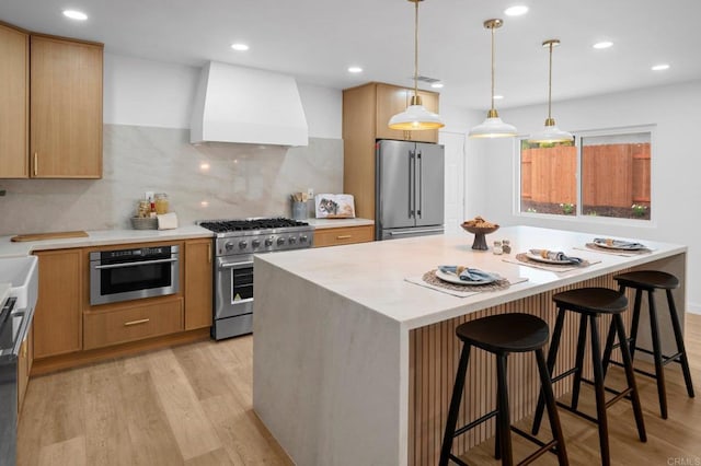 kitchen with high end appliances, light wood-style flooring, a breakfast bar area, light countertops, and premium range hood