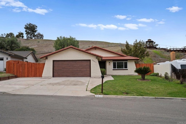 view of front of house with stucco siding, an attached garage, a front yard, fence, and a tiled roof