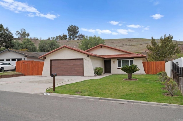 ranch-style house featuring concrete driveway, a tiled roof, an attached garage, fence, and a front yard