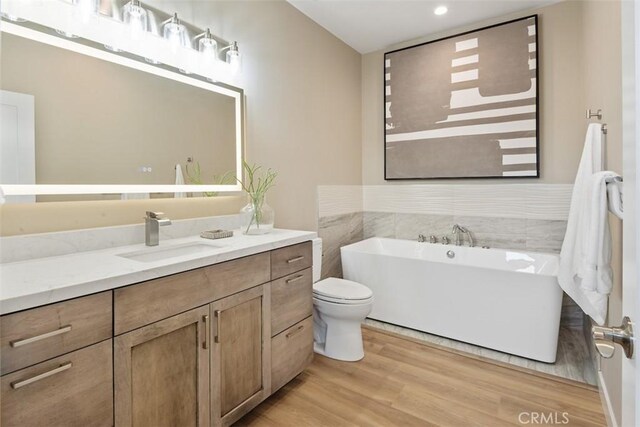 full bath with toilet, a freestanding tub, wood finished floors, and vanity