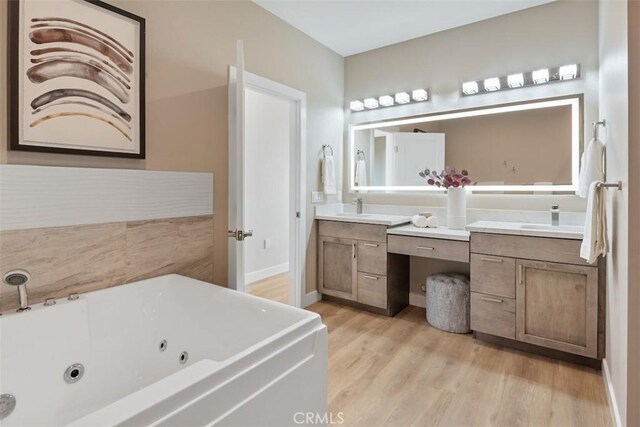 full bathroom with a jetted tub, wood finished floors, vanity, and baseboards