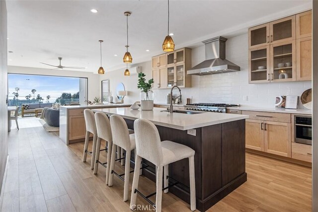 kitchen with light wood-style flooring, light countertops, wall chimney range hood, stainless steel oven, and backsplash