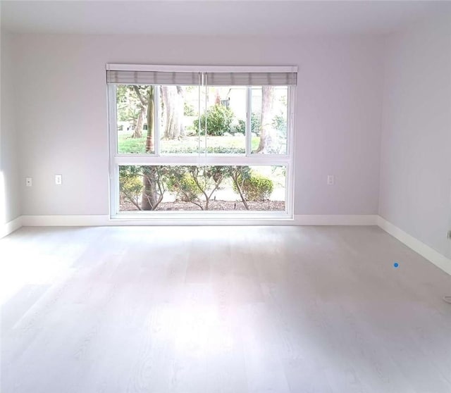 empty room featuring a healthy amount of sunlight, baseboards, and wood finished floors