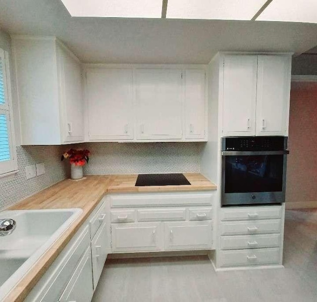 kitchen with a sink, black cooktop, wall oven, and white cabinets