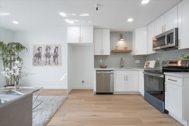 kitchen featuring a sink, stainless steel appliances, light wood-style floors, white cabinetry, and backsplash