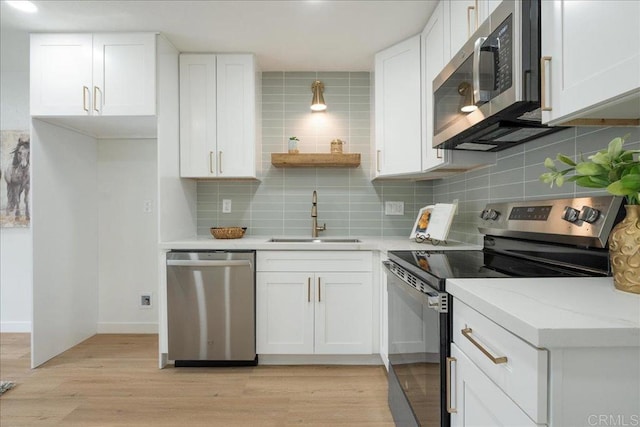 kitchen with appliances with stainless steel finishes, light wood-type flooring, white cabinets, and a sink