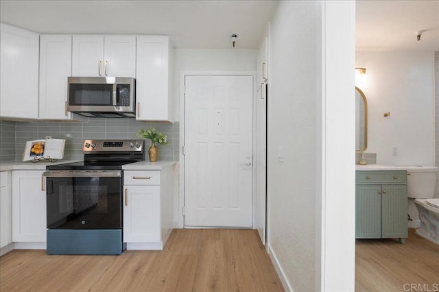 kitchen with light wood finished floors, white cabinets, decorative backsplash, appliances with stainless steel finishes, and light countertops