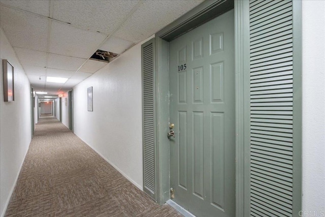 hall with carpet, a paneled ceiling, and baseboards