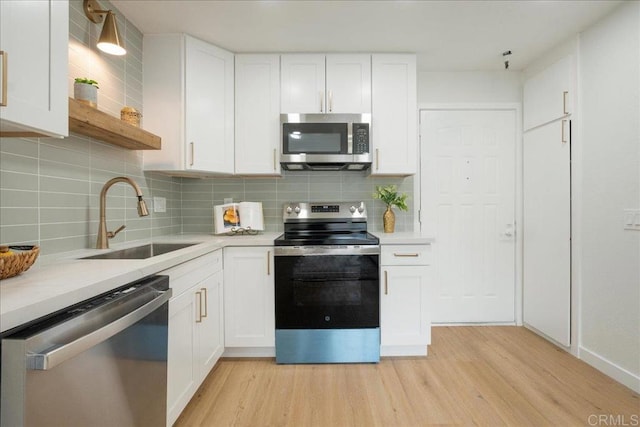 kitchen with stainless steel appliances, light countertops, white cabinetry, a sink, and light wood-type flooring