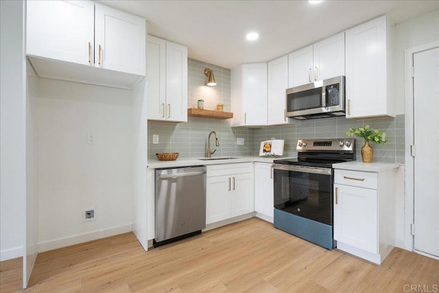 kitchen featuring light wood-style flooring, appliances with stainless steel finishes, a sink, light countertops, and backsplash