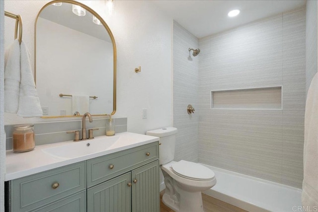 bathroom featuring vanity, a tile shower, and toilet