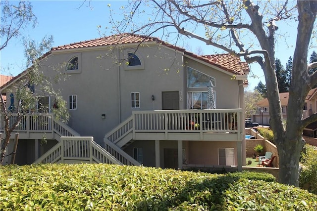 rear view of house with a deck, a tile roof, stairway, and stucco siding