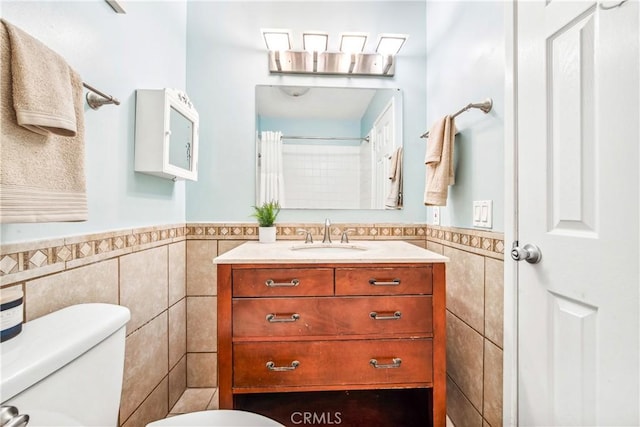 full bath featuring toilet, a wainscoted wall, tile walls, and vanity