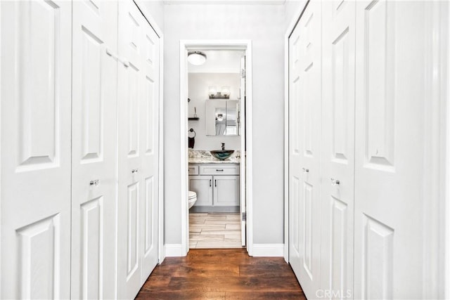 hallway with dark wood-style floors, a sink, and baseboards