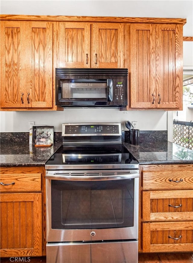 kitchen with brown cabinetry, dark stone counters, electric stove, and black microwave