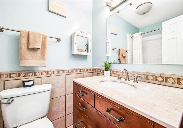 bathroom featuring toilet, a wainscoted wall, a shower with curtain, vanity, and tile walls