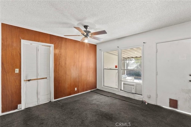 carpeted spare room featuring cooling unit, wooden walls, a ceiling fan, and a textured ceiling