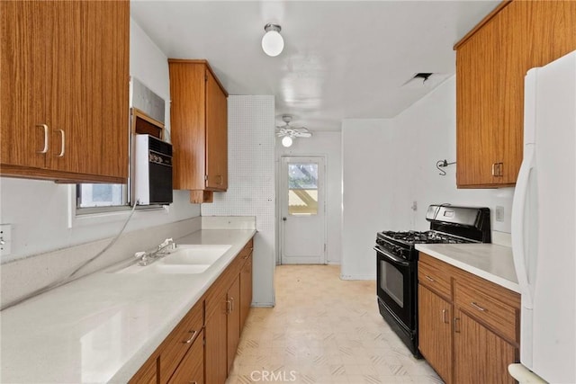 kitchen with black gas range, a sink, freestanding refrigerator, brown cabinetry, and light floors