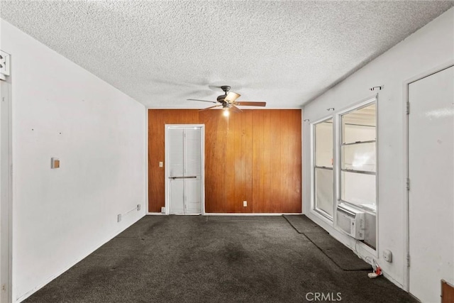 carpeted empty room featuring cooling unit, a textured ceiling, wood walls, and a ceiling fan