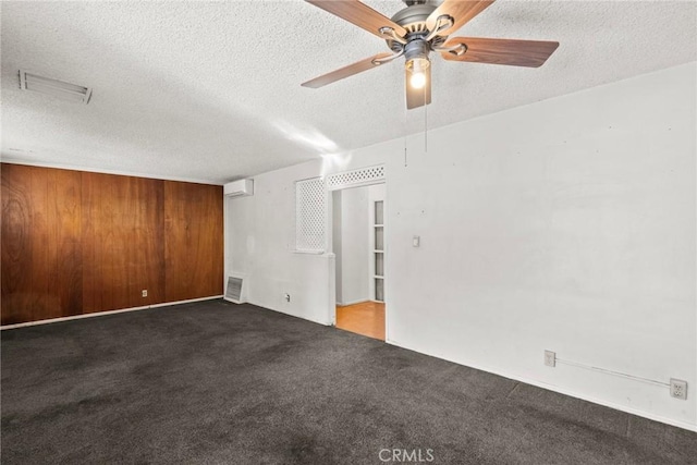 unfurnished room featuring wooden walls, carpet flooring, visible vents, and a textured ceiling