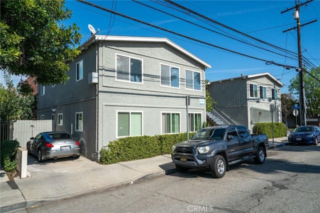 view of front facade with fence, stairway, and stucco siding