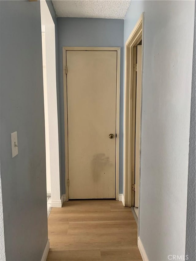 hallway featuring light wood-type flooring, a textured ceiling, and baseboards