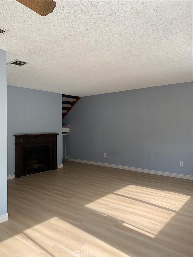 unfurnished living room with visible vents, a fireplace, baseboards, and wood finished floors