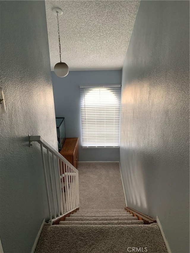 stairway featuring a textured ceiling, a textured wall, carpet flooring, and baseboards