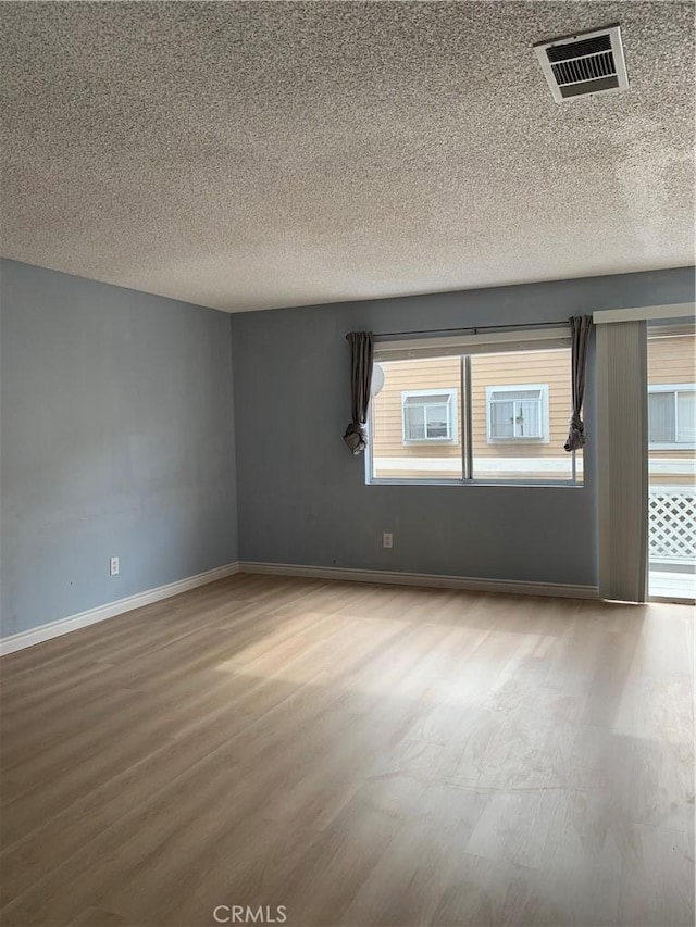 empty room with a textured ceiling, wood finished floors, visible vents, and baseboards