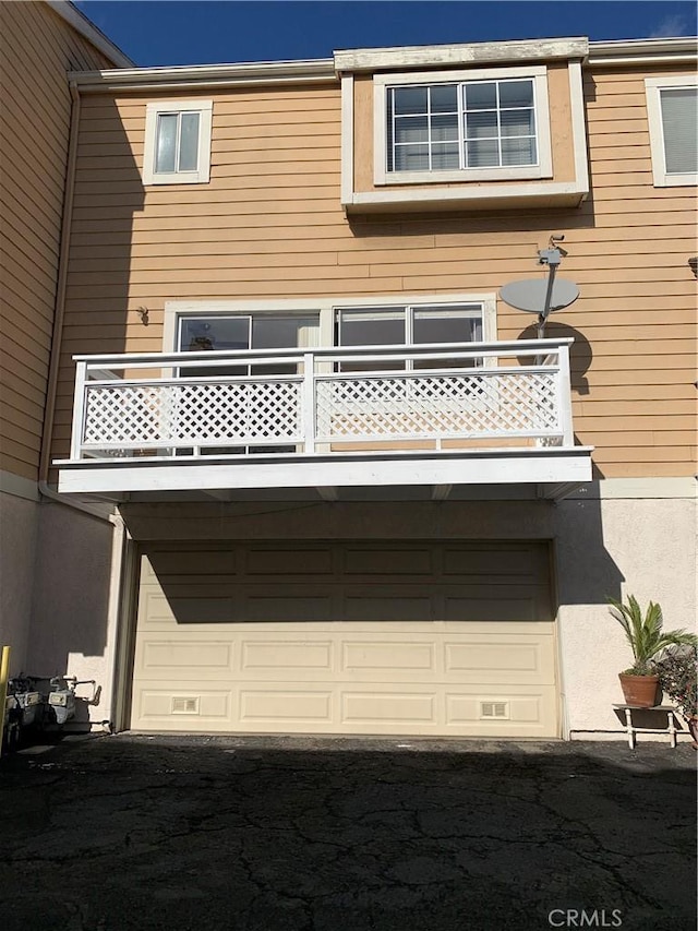 back of property featuring an attached garage, a balcony, and stucco siding